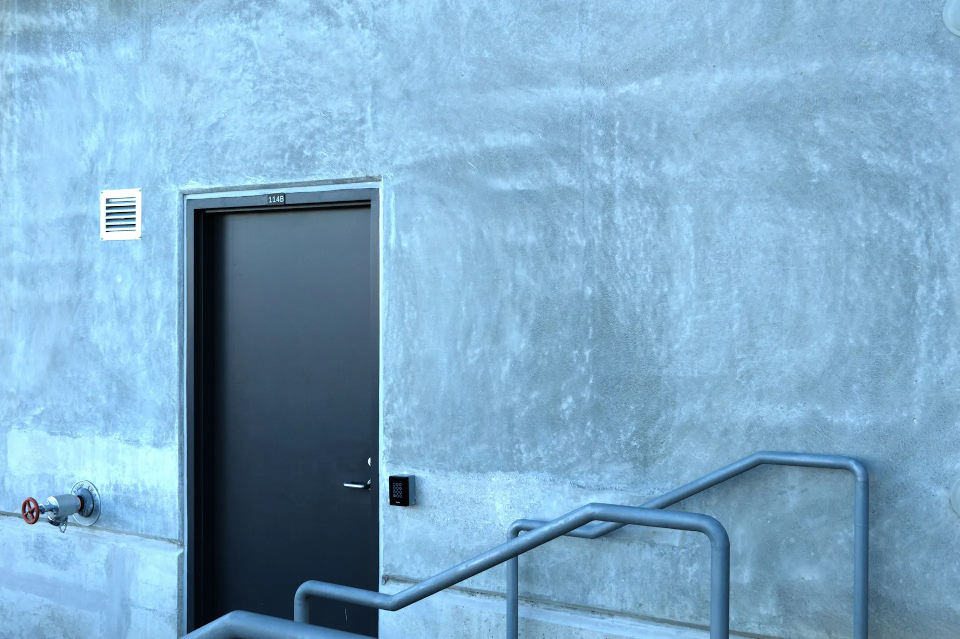 Moderne Hauseingangstür in grauer Wand mit Treppenhandlauf