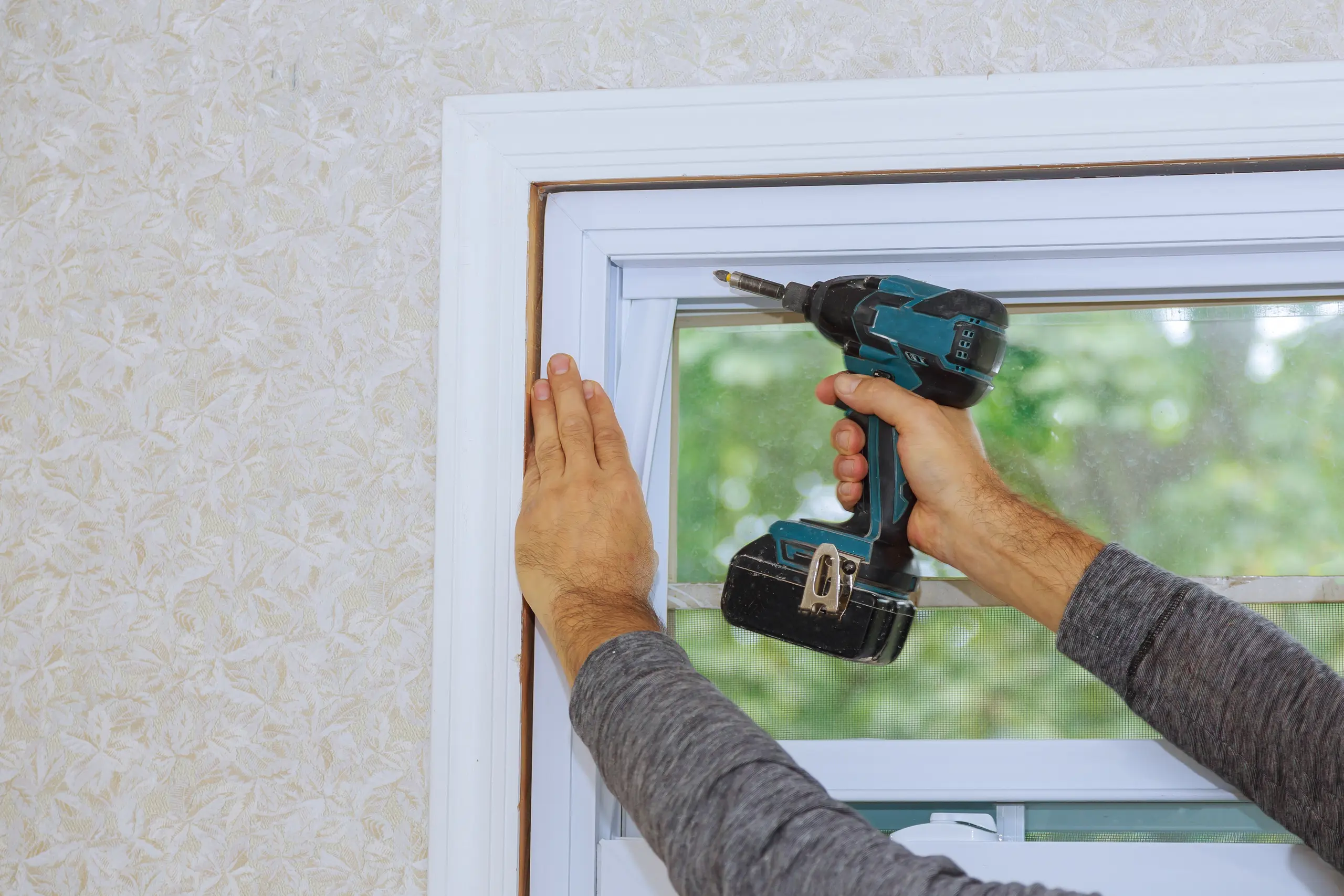 Ein Handwerker installiert ein PVC Fenster mit einer Bohrmaschine
