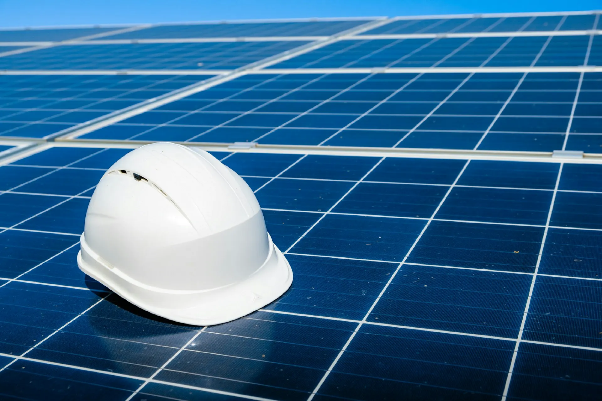 Ein weißer Helm liegt auf Solarzellen, die Installation von Solaranlagen wird dargestellt